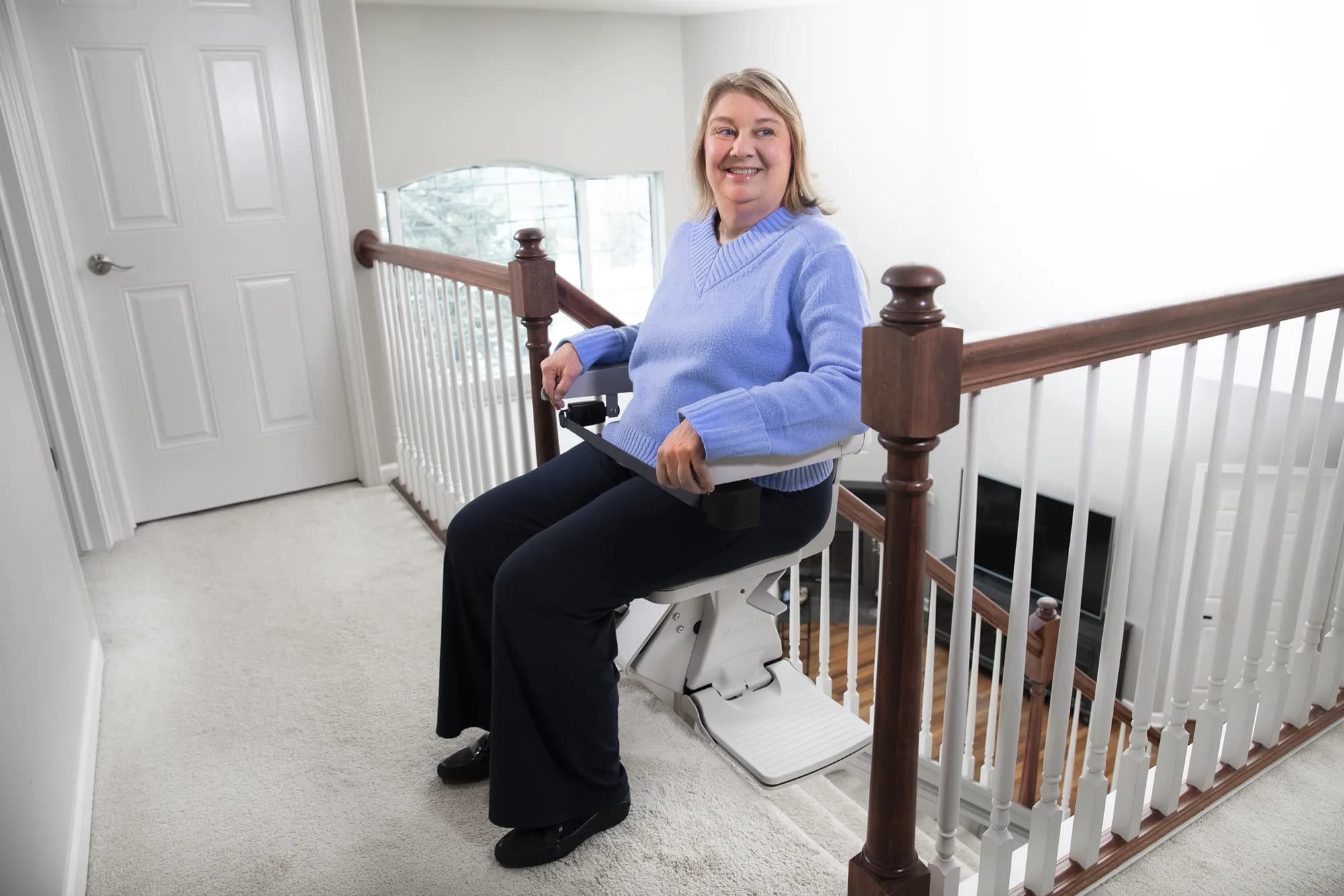 Woman seated on a Bruno Elan SRE-5000 stairlift at the top landing with the seat swiveled toward the hallway