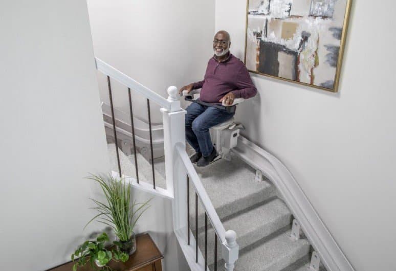 Man seated on a Bruno Elite SRE-2010 stairlift riding up an indoor staircase
